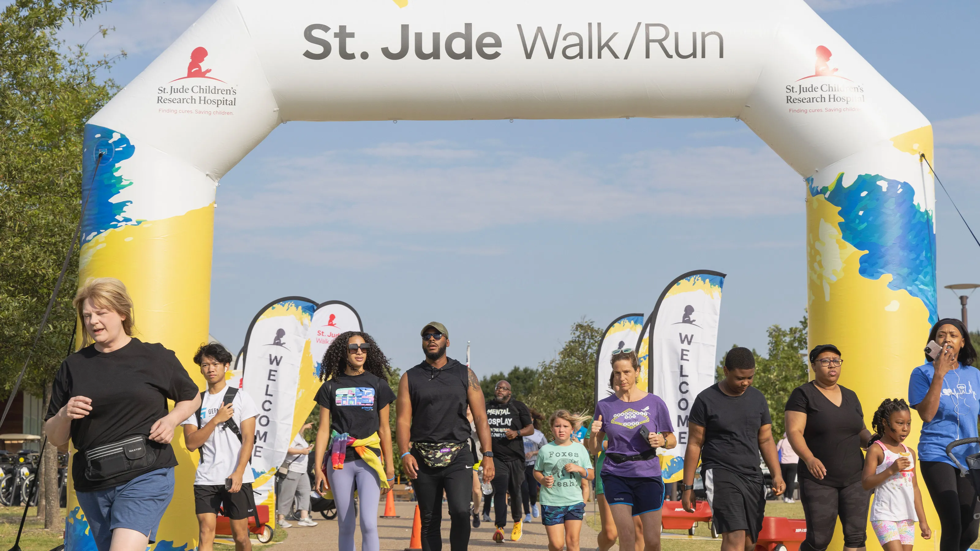 Participants run under St. Jude Walk/Run arch with welcome banners in background.
