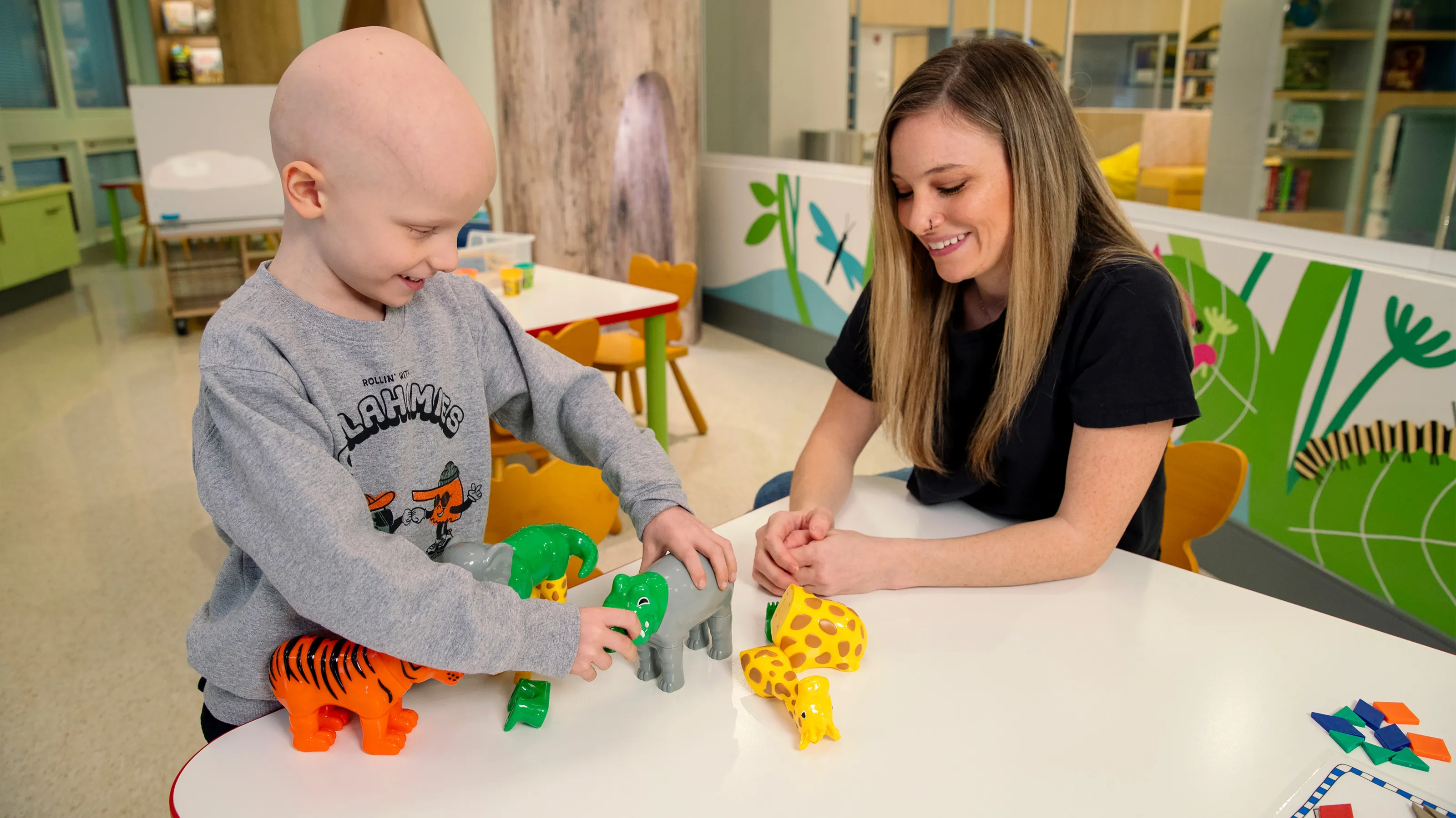 A child and an adult playing with plastic animal toys at a table in a bright room.
