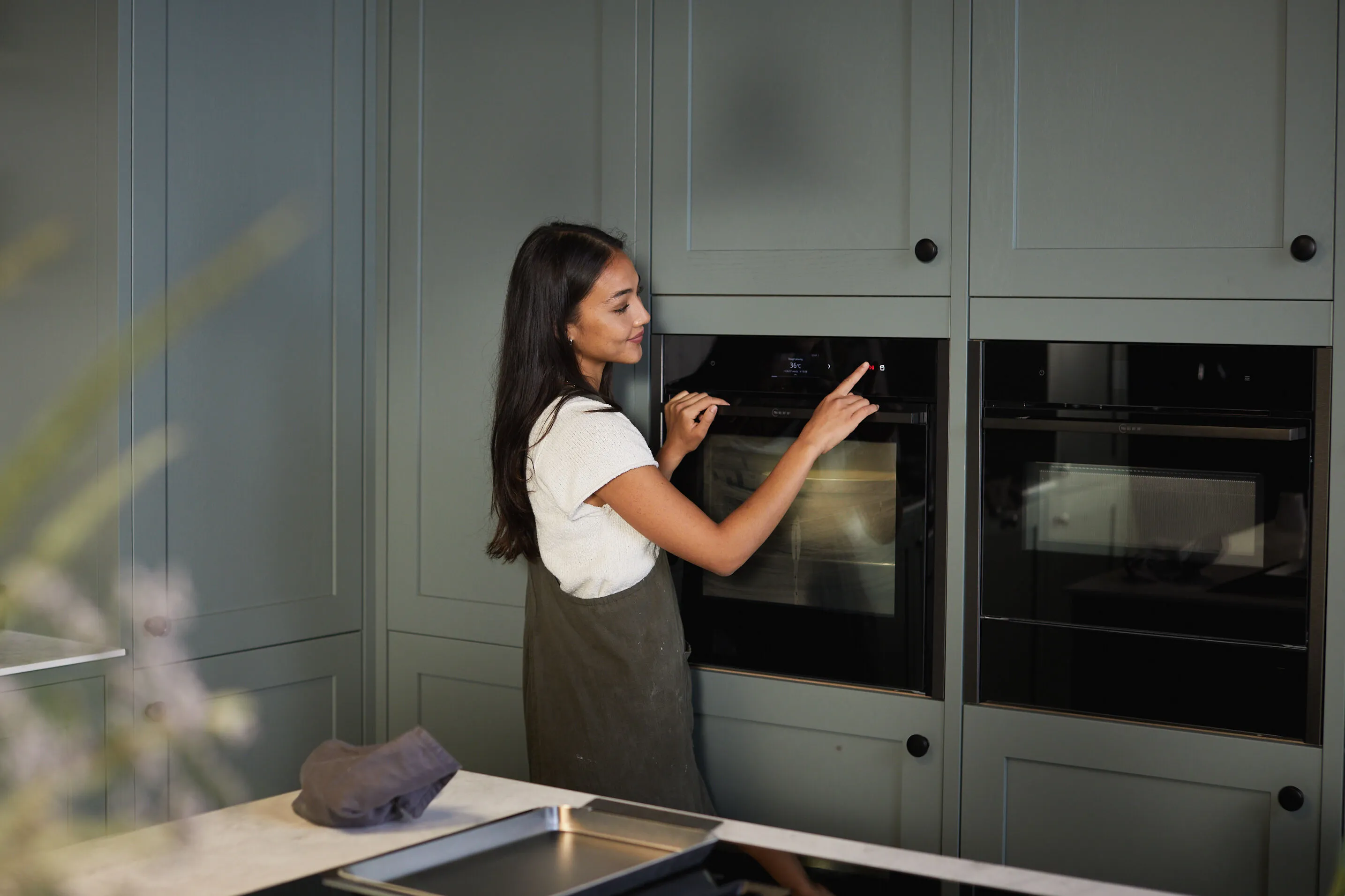 Donna in cucina con forno, armadi grigi, elettrodomestici da cucina.