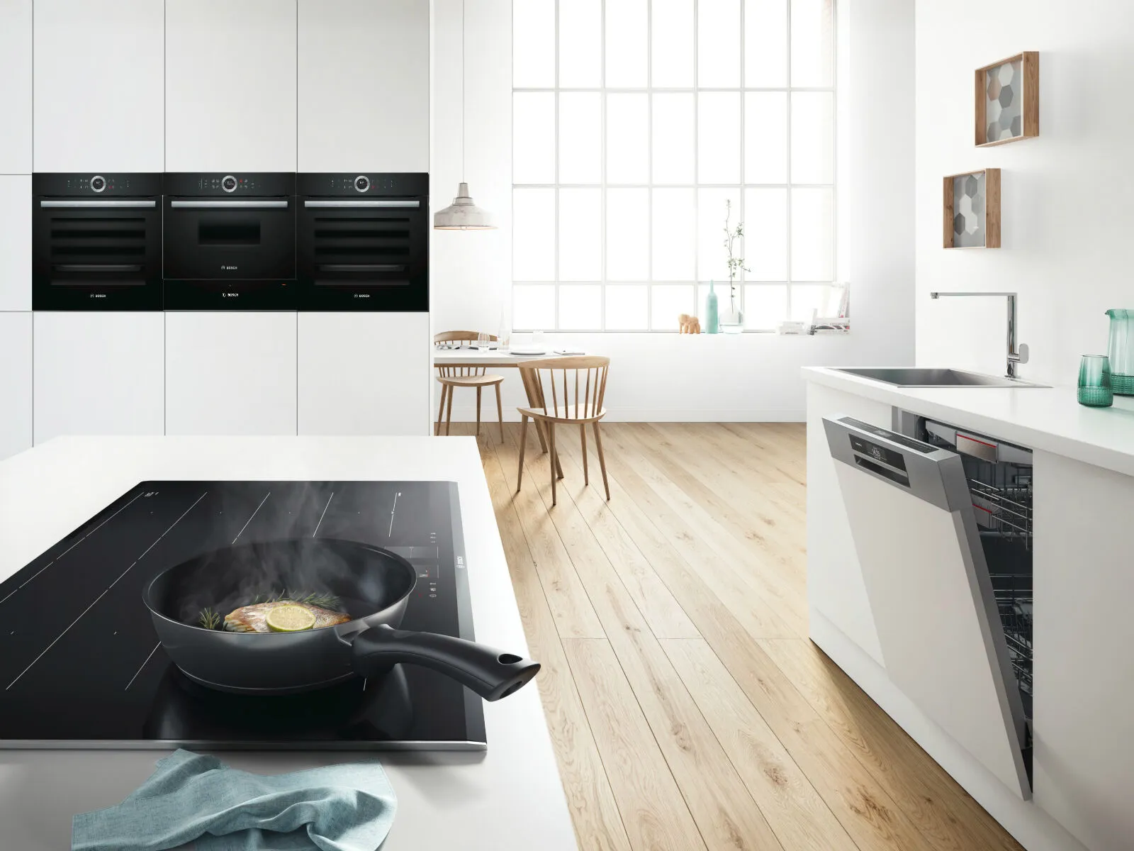 Modern kitchen with white cabinets, black appliances, wooden table, and large window.
