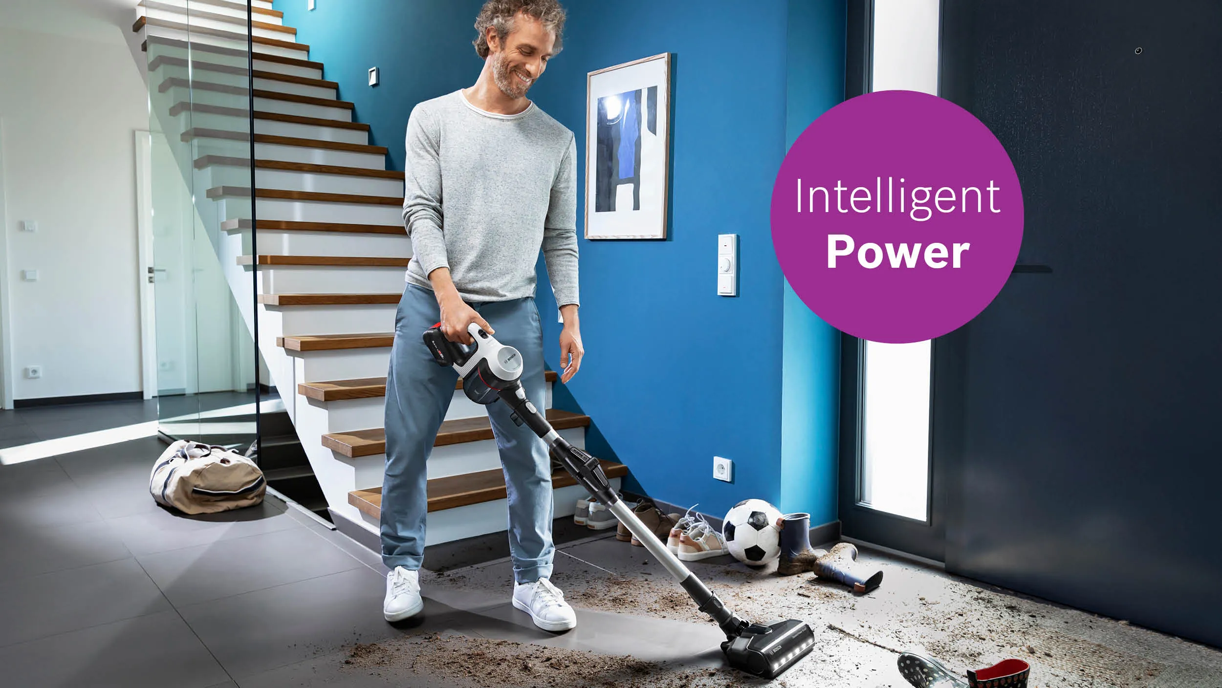 Man using vacuum cleaner in home with soccer ball and "Intelligent Power" text overlay.