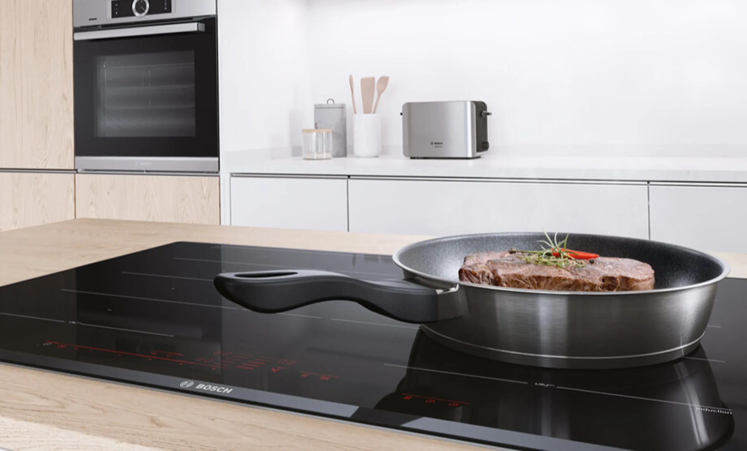 Modern kitchen with induction cooktop, oven, and cooking utensils on countertop.