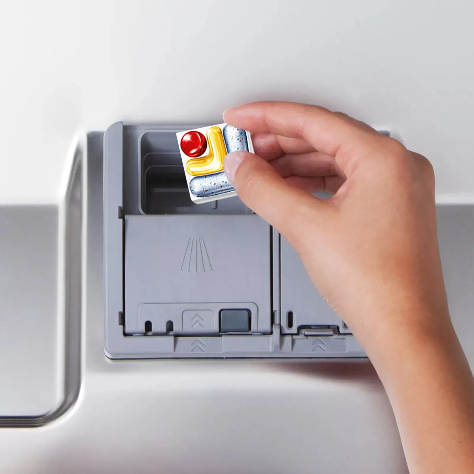Hand placing a dishwasher tablet in the detergent compartment inside the dishwasher door.