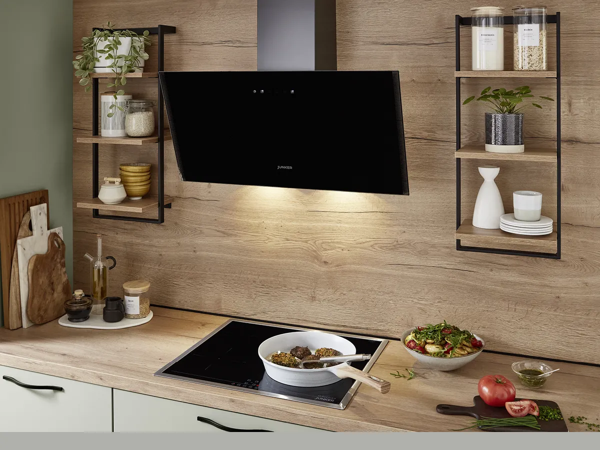 A black Junker extractor hood above a Junker cooktop with a pan of food cooking on it.