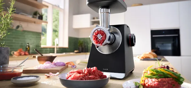 Billedet viser en sort Bosch kødhakker der har hakket kød i en stor glasskål .
