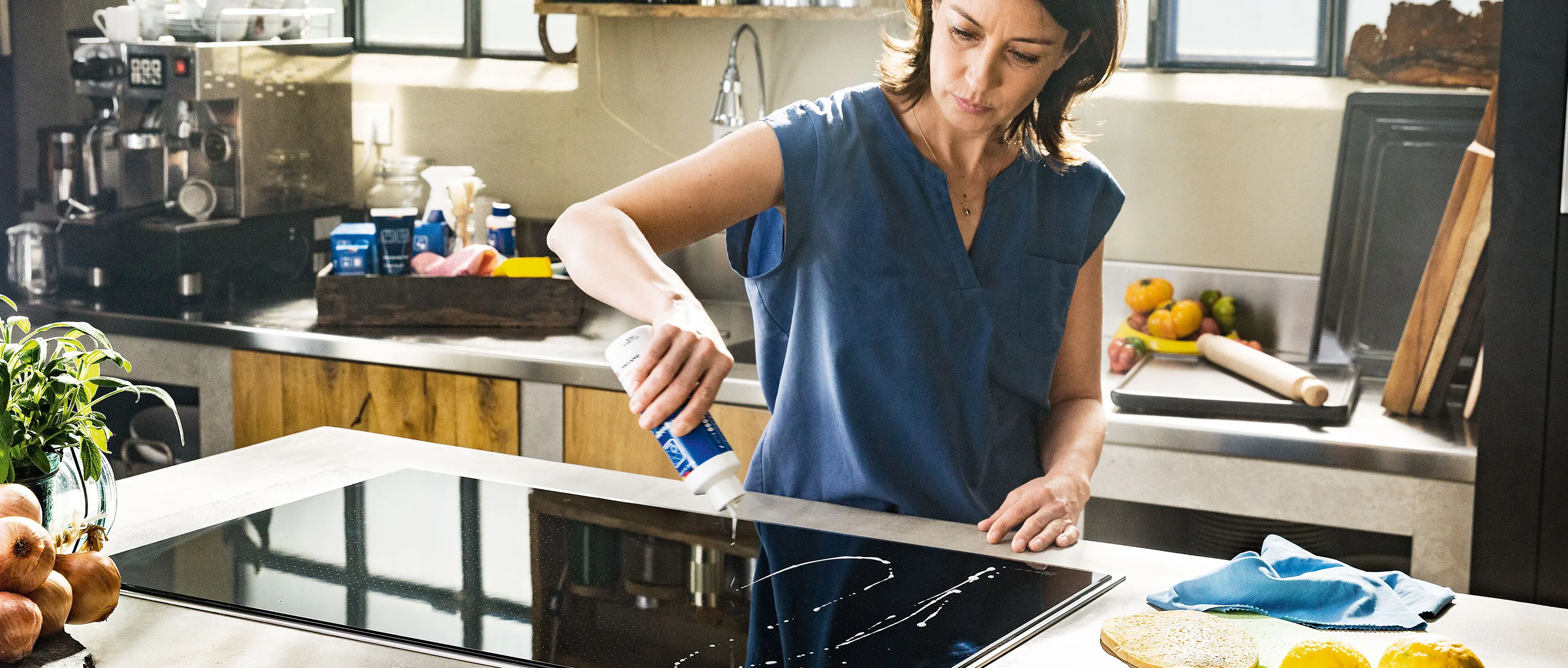 Lady in a kitchen cleaning induction hob with a NEFF tested cleaning product.