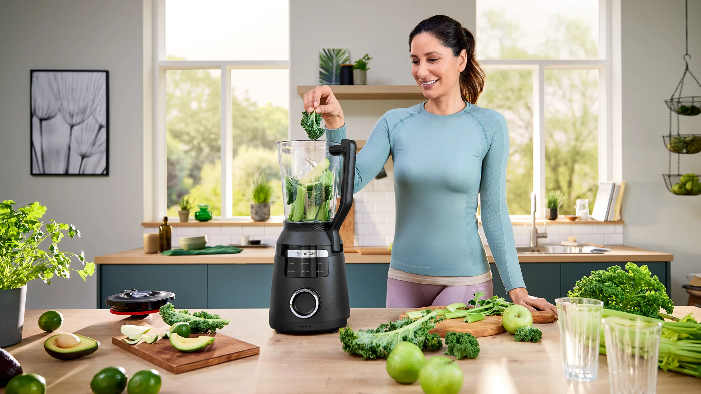 Femeie care umple un blender Bosch VitaPower Serie 6, de pe blatul din bucătărie, cu legume verzi, precum varză Kale, mere verzi, avocado şi ţelină.