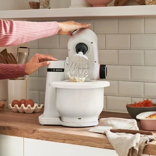 Bosch stand mixer with a whisk next to a cake and whipped cream.
