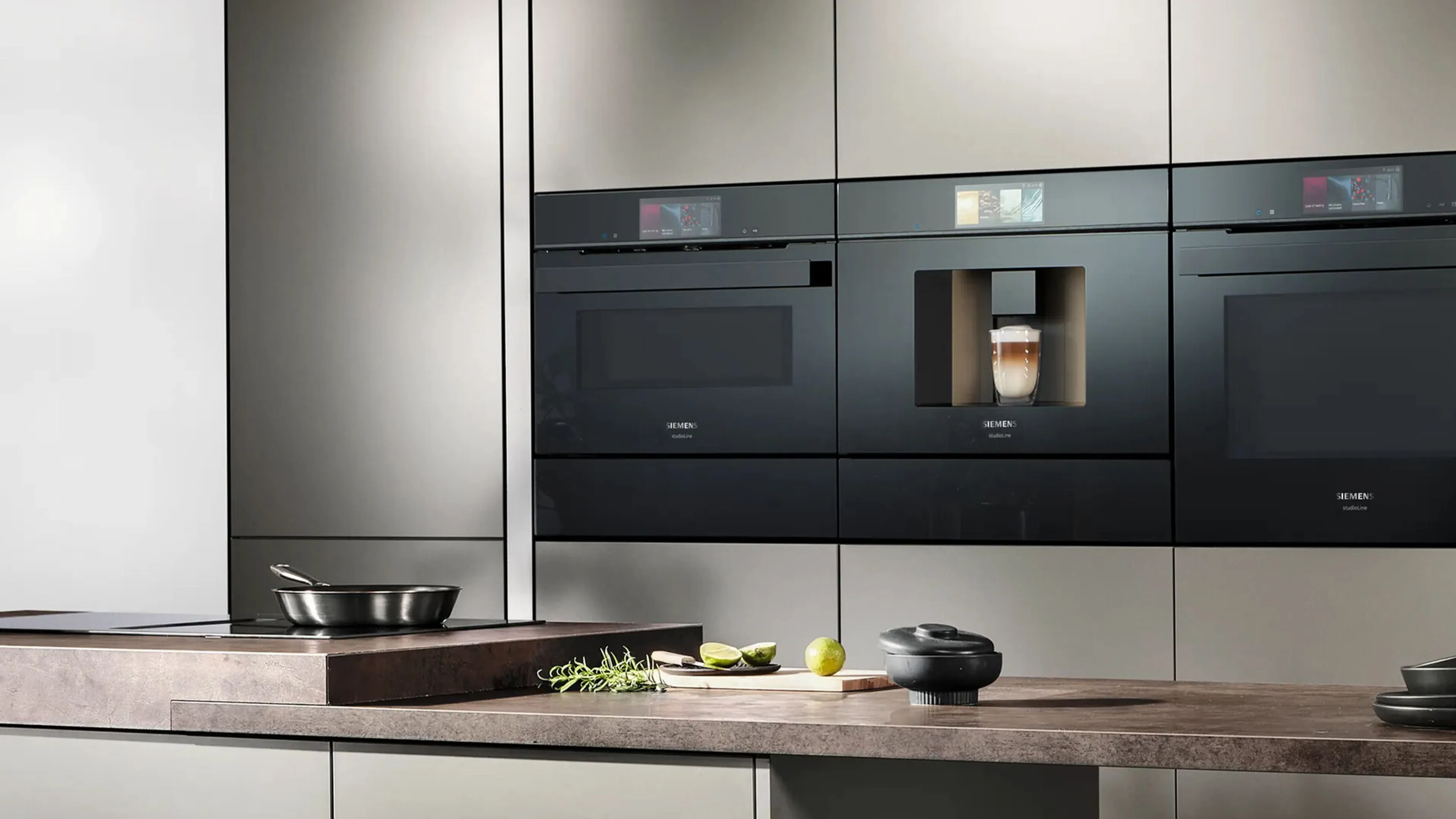 Modern kitchen featuring sleek black built-in ovens against a warm wooden backdrop, with a cozy living area visible in the background.