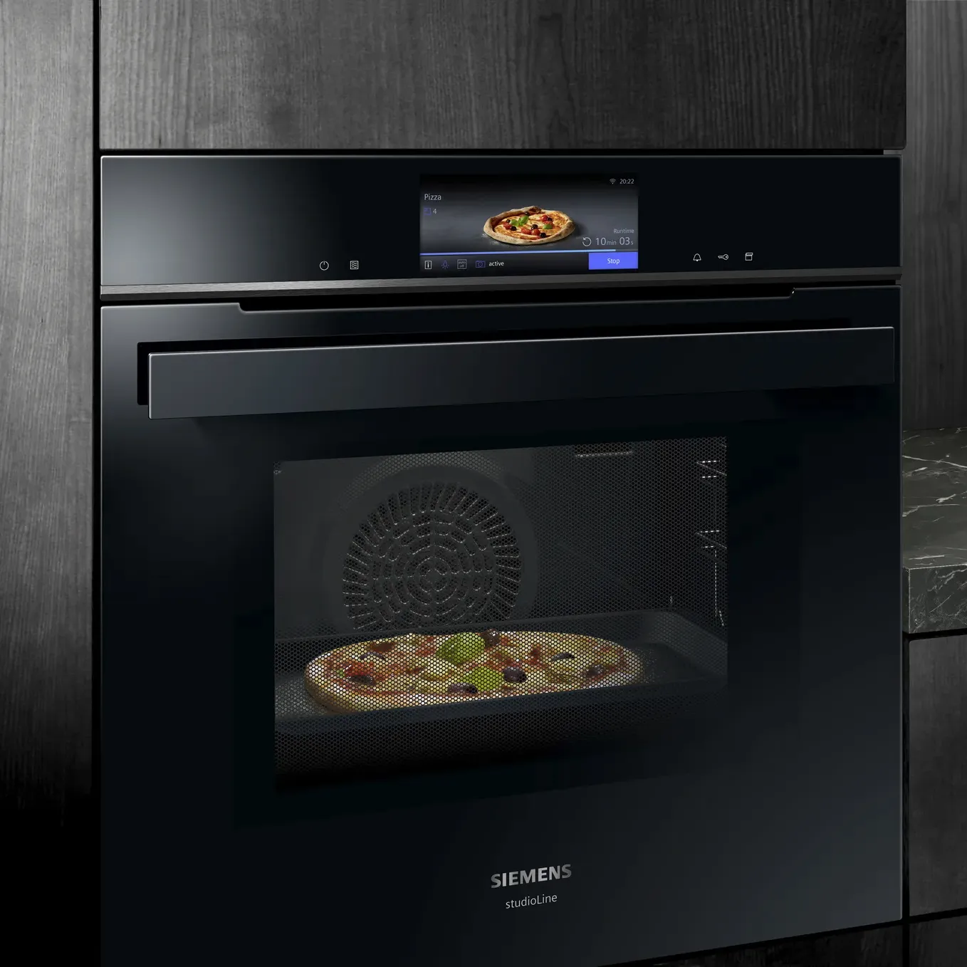 Un four Siemens noir élégant avec écran tactile, affichant une pizza à l’intérieur, sur fond d’une cuisine sombre.