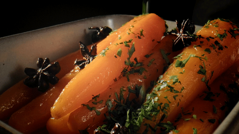 Star anise glazed carrots in roasting dish with herbs sprinkled on top