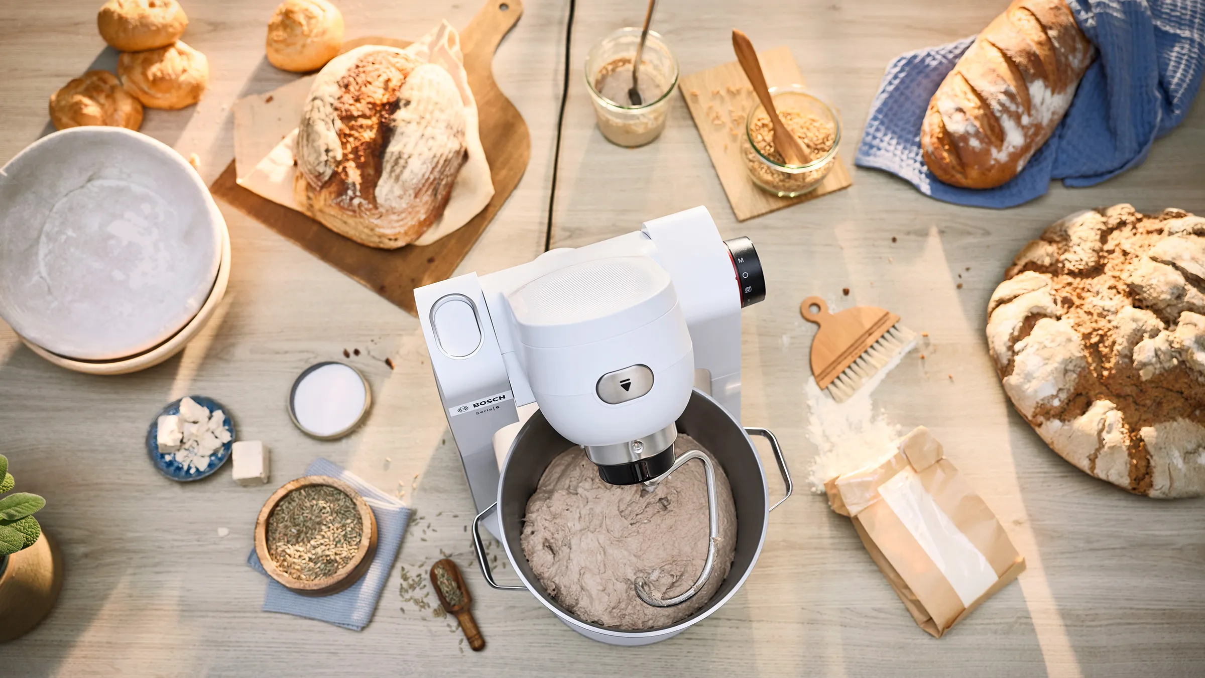 Fågelperspektiv av Serie 6 köksmaskin som knådar deg omgiven av olika brödlimpor, salt, peppar och jäst på köksbänk.
