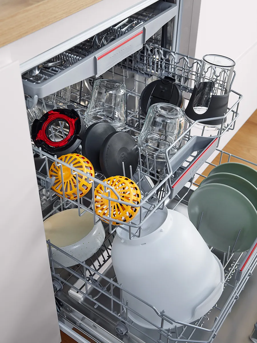 Vaatwasser met verschillende onderdelen van de keukenrobot, waaronder plastic kom, schijfhouders en kannen.