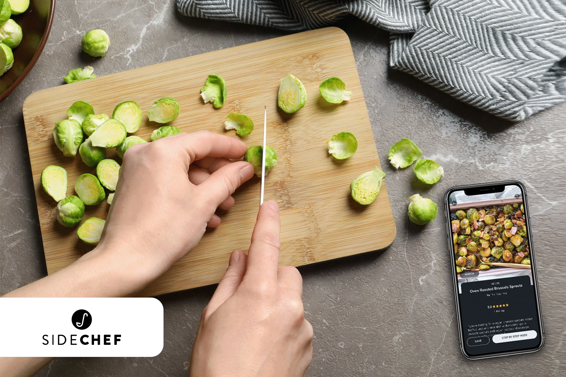 Person slicing Brussels sprouts on a wooden board next to a smartphone displaying a recipe.