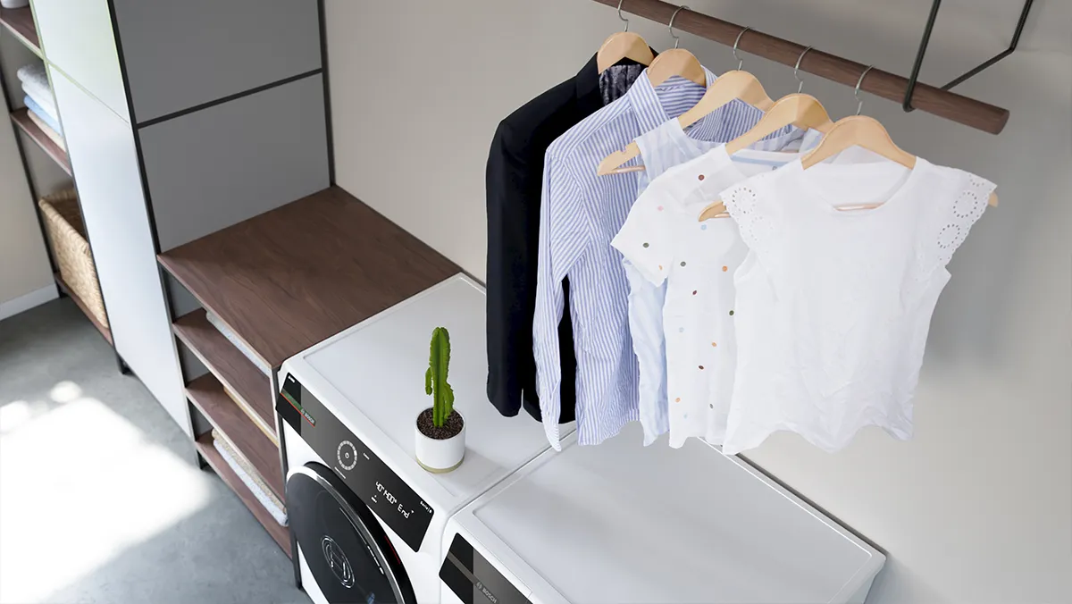 Ett modernt tvättrum med ett torkställ med prydligt upphängda skjortor och blusar, tillsammans med tvättmaskin, torktumlare och en liten kaktus. 