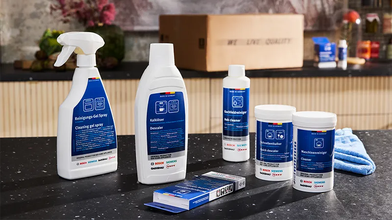 alt-A selection of  cleaning products on a kitchen counter, including sprays and powders for various surfaces, with a blue cloth beside them.