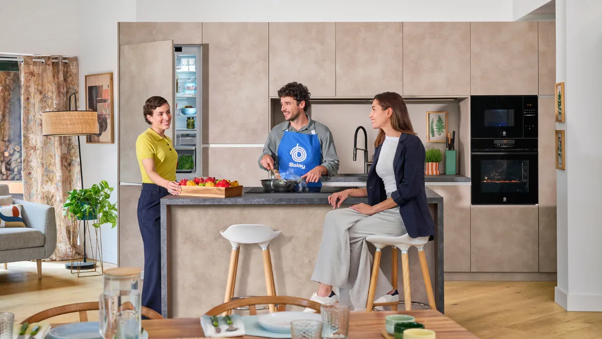 Tres personas en una cocina moderna, preparando comida y conversando.