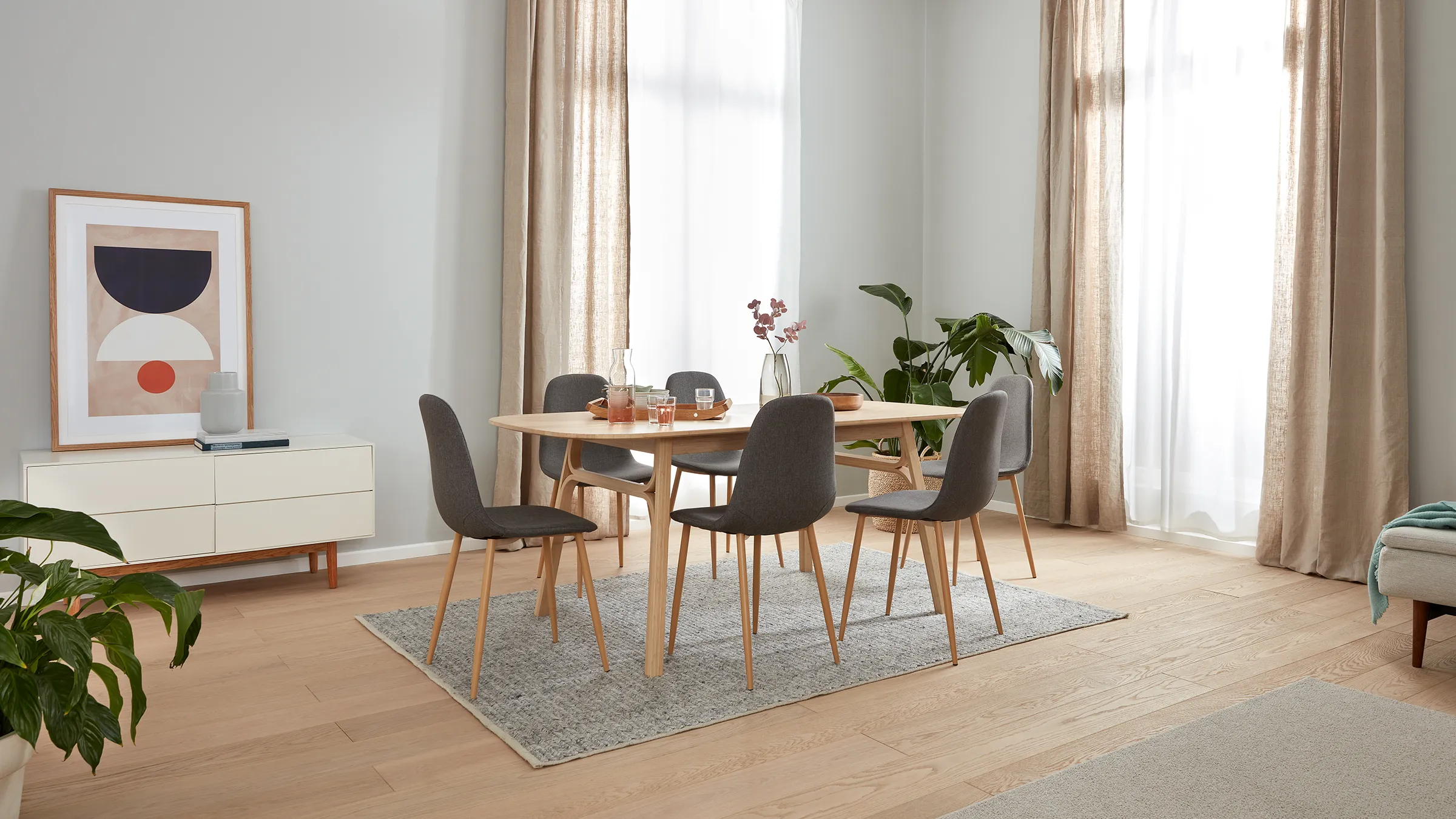 Ahşap masa, gri sandalyeler, sanat ve büyük pencereye yakın bitkilerle Minimalist yemek odası.