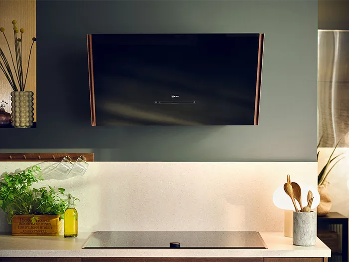 Modern kitchen with mounted hood, potted plants, and cooking utensils on countertop.