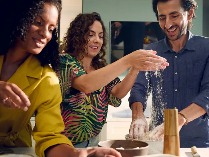 Three people cooking together, smiling and having fun in the kitchen.