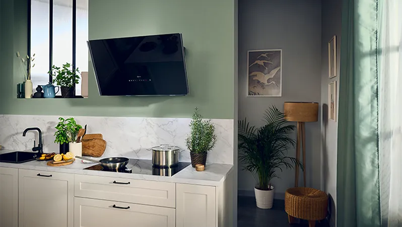 Modern kitchen with white cabinets, marble backsplash, herbs and cookware on the counter; small seating nook with plant and lamp.