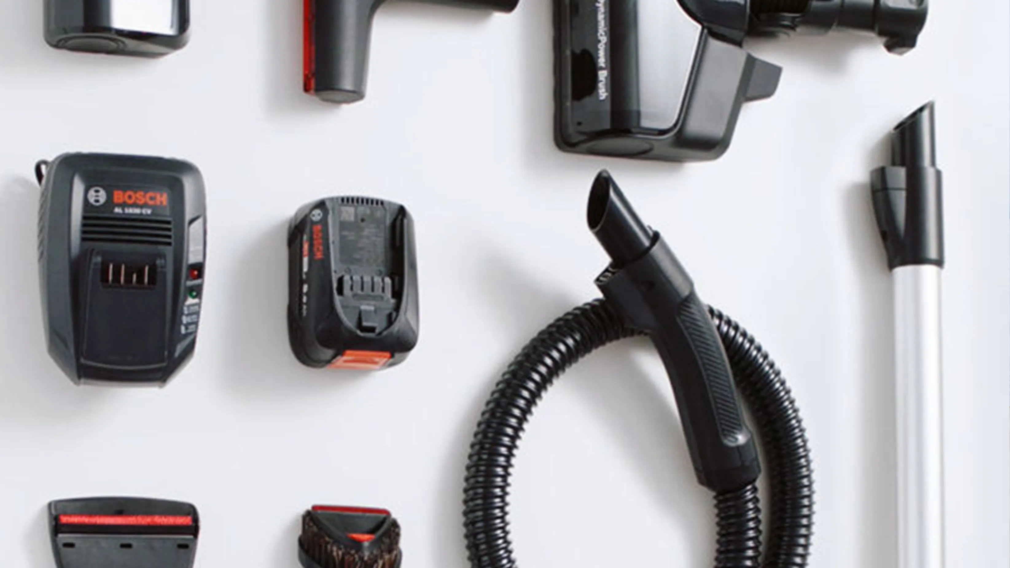 Uspořádání příslušenství vysavače včetně hadice, baterie, nabíječky a různých nástavců na nářadí na bílém pozadí.