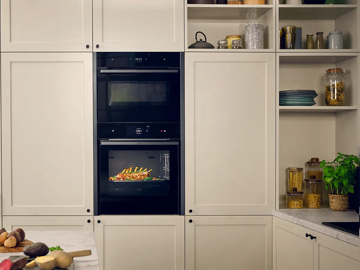 Modern kitchen with white cabinets, built-in oven, shelves with kitchenware, and fresh produce on the counter.