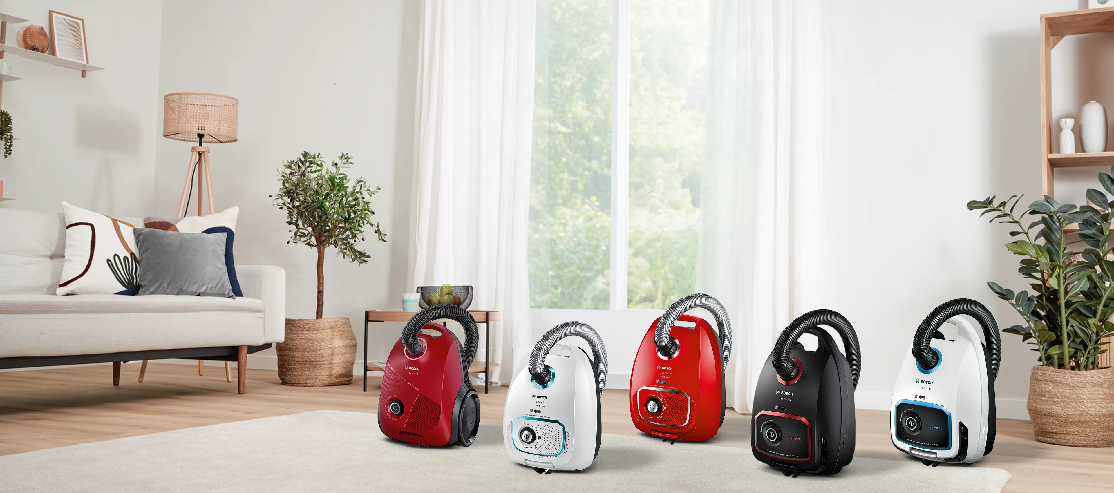 Two Bosch vacuum cleaners in navy blue and black beside a light-colored rug in a bright, modern living room.
