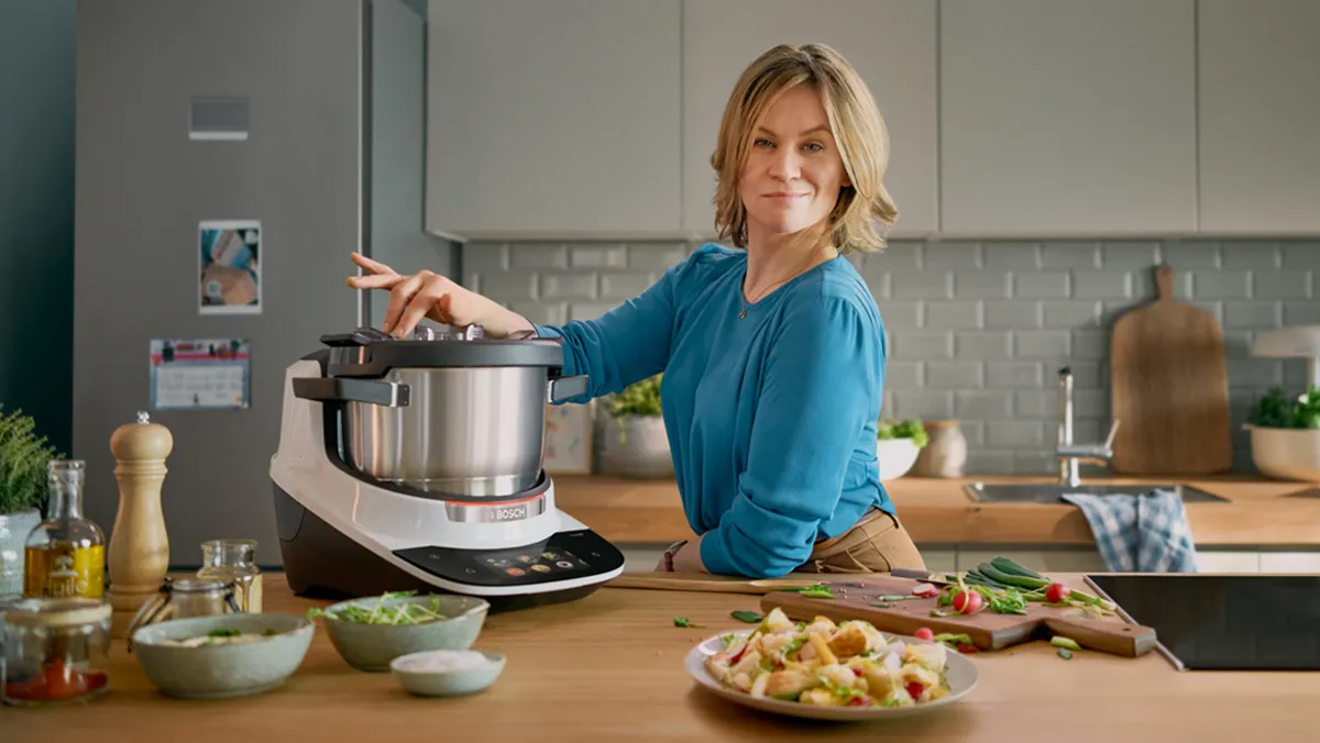 Donna che cucina in cucina utilizzando un robot da cucina, preparando un pasto sano con ingredienti freschi.