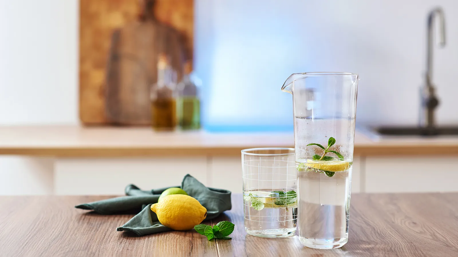 Glas und Karaffe mit Wasser, Zitrone und Minze auf einem Küchentisch.
