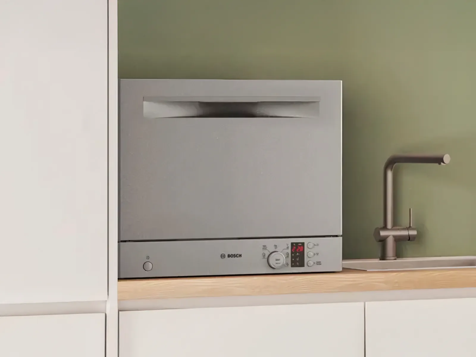 Silverfärgad kompakt fristående diskmaskin på bänkskivan.