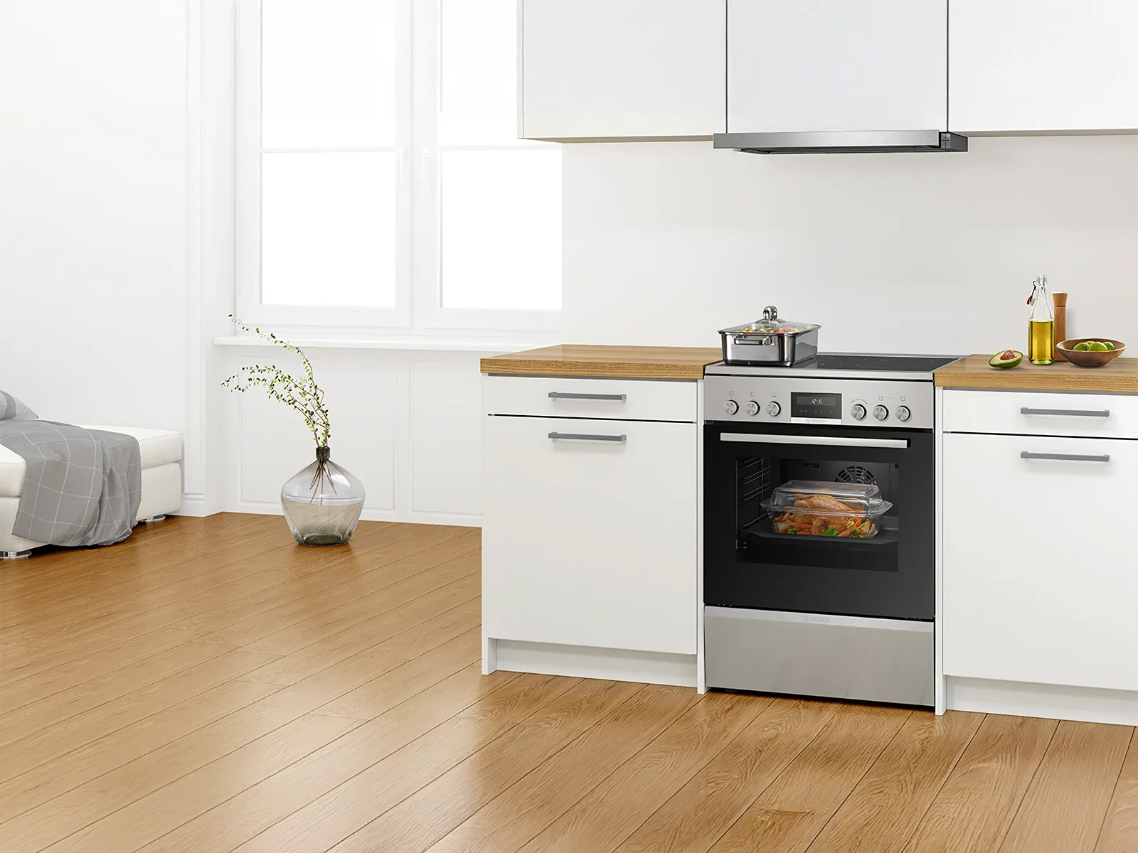 Freestanding cooker with an induction hob and multifunctional oven, featuring a glass dish of roasted chicken and vegetables.