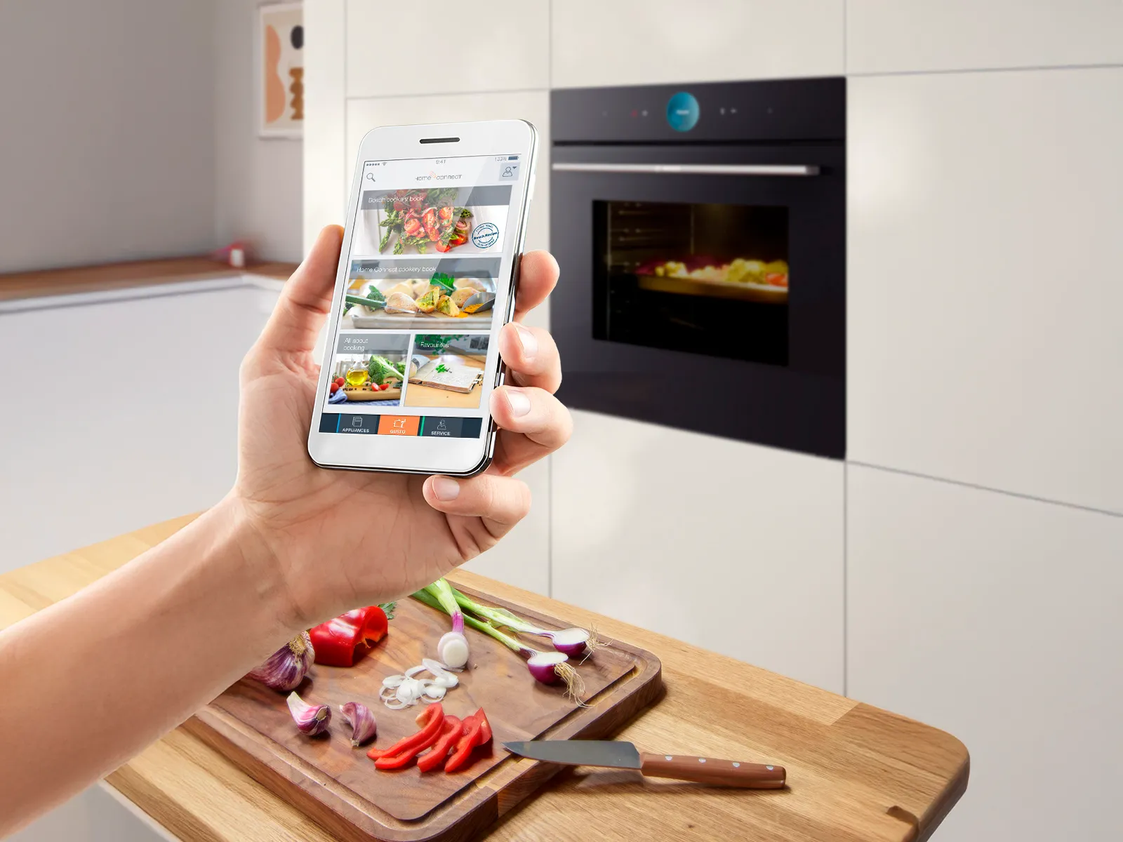 Mână care ține un smartphone cu rețete de mâncare, fundal de bucătărie cu legume pe tocător.