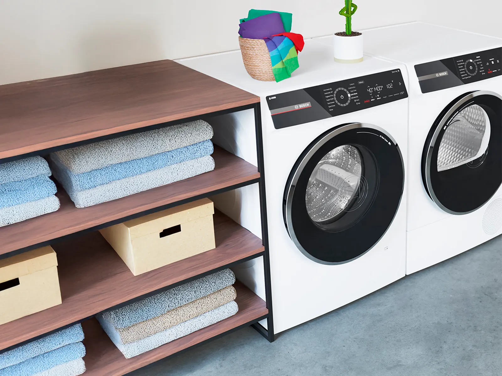 Moderne Waschmaschine und Trockner neben einem Holzregal mit Handtüchern und einer Pflanze.