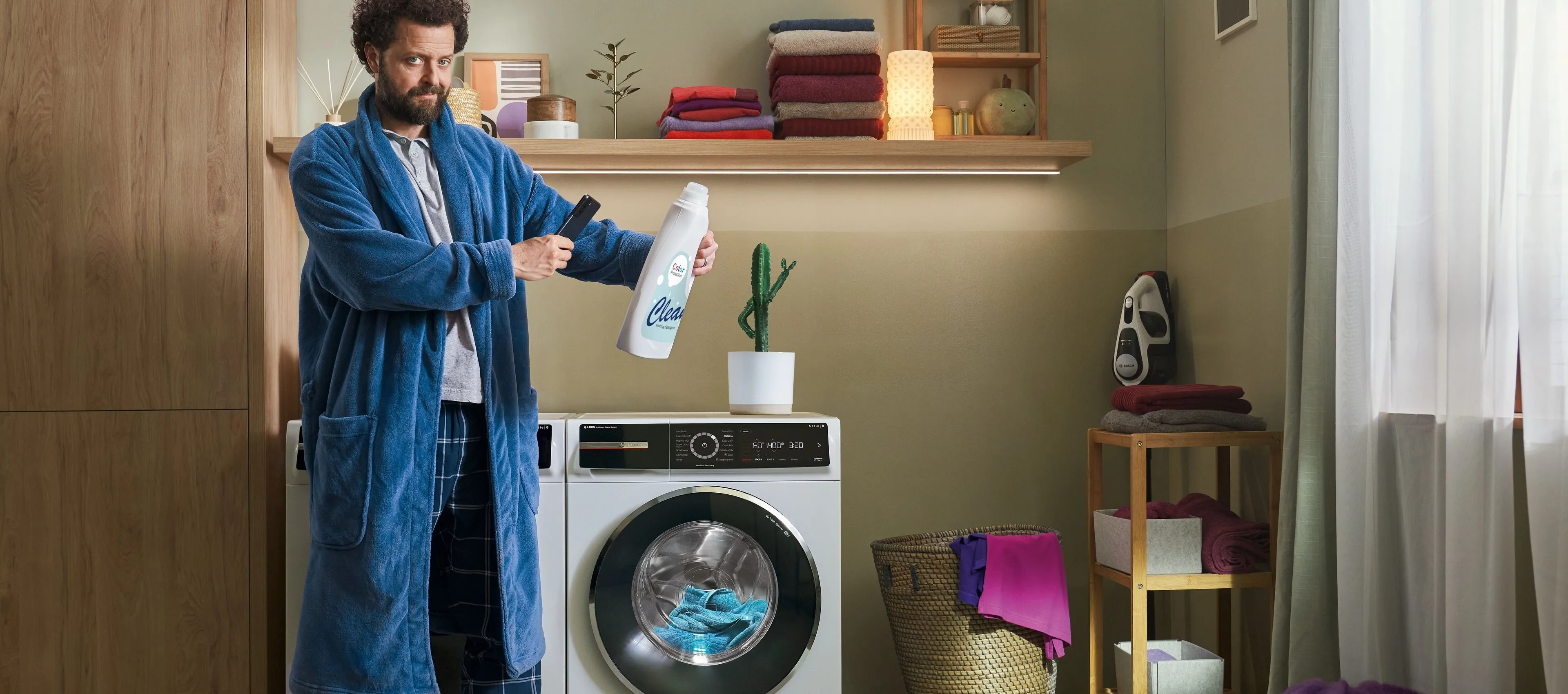 Ένας άντρας όπου κρατάει ένα απορρυπαντικό κι στέκεται δίπλα από ένα πλυντήριο.