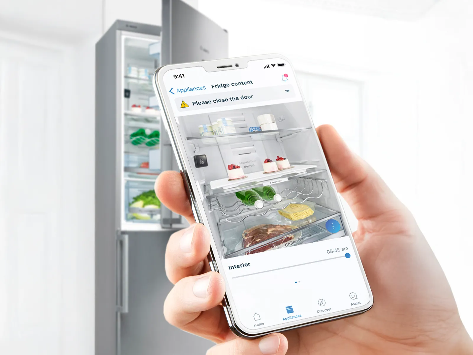 Nyissa meg a telefont a Home Connect alkalmazáshoz. Egy hűtőszekrény a háttérben.