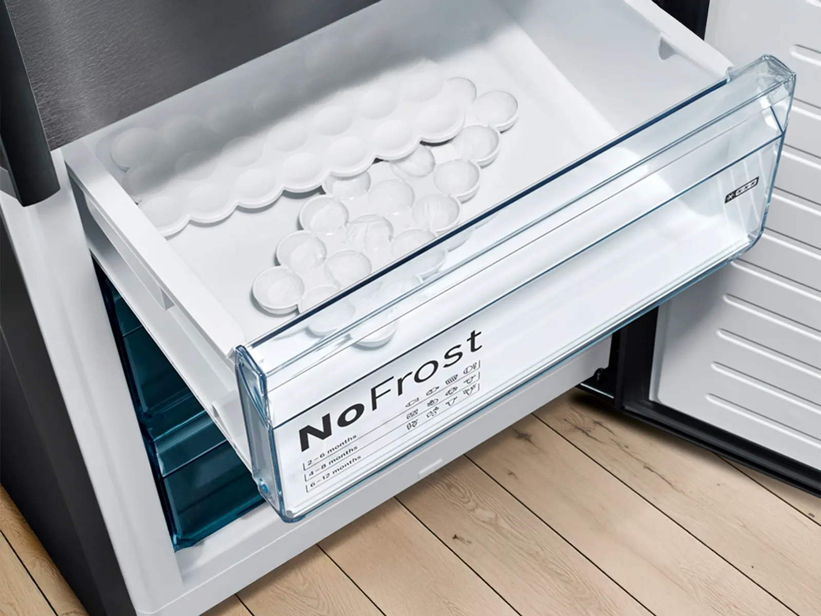 Tiroir de congélateur ouvert avec l'étiquette "NoFrost", des bacs à glaçons à l'intérieur, sur un sol en bois.