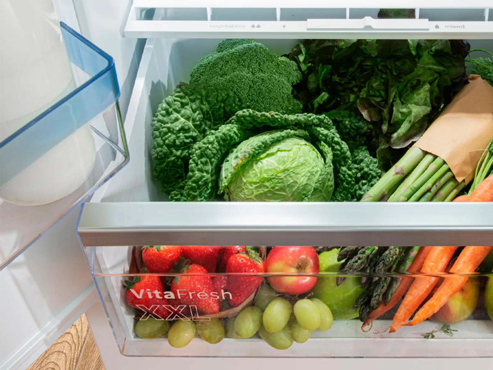 Réfrigérateur-congélateur ouvert avec tiroir, rempli d'ingrédients frais.