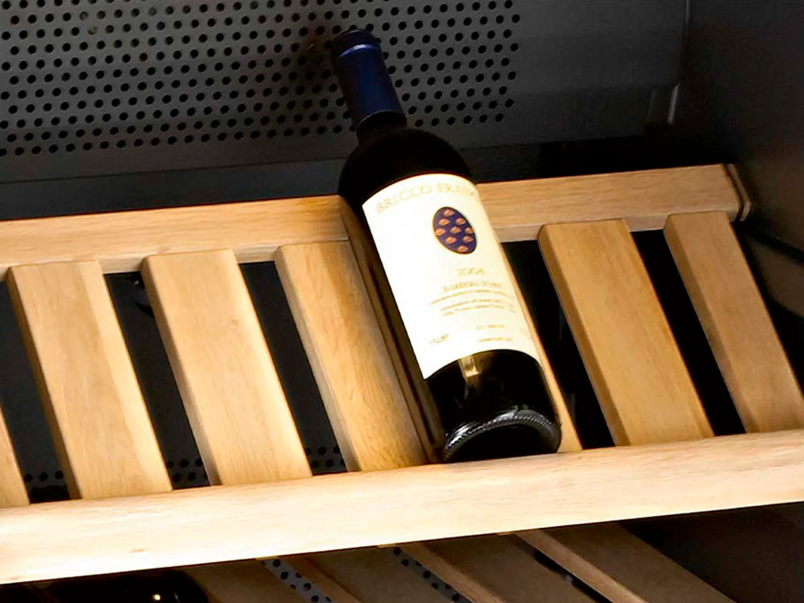 A bottle of red wine on a wooden shelve inside a wine cooler.