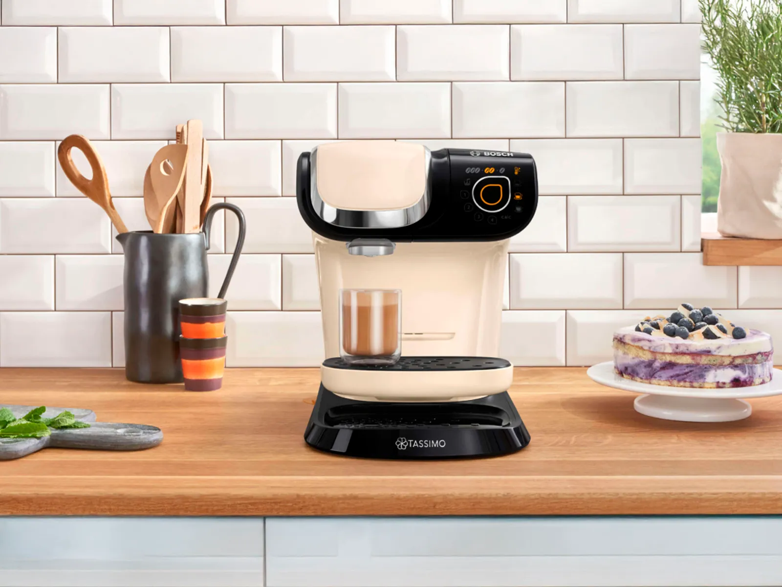 La macchina da caffè TASSIMO MYWAY 2 con un Cortado sul piano di lavoro di una cucina e una torta accanto.