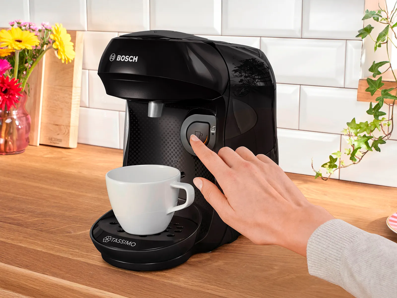 A person clicks on the TASSIMO HAPPY friendly coffee machine's start button.