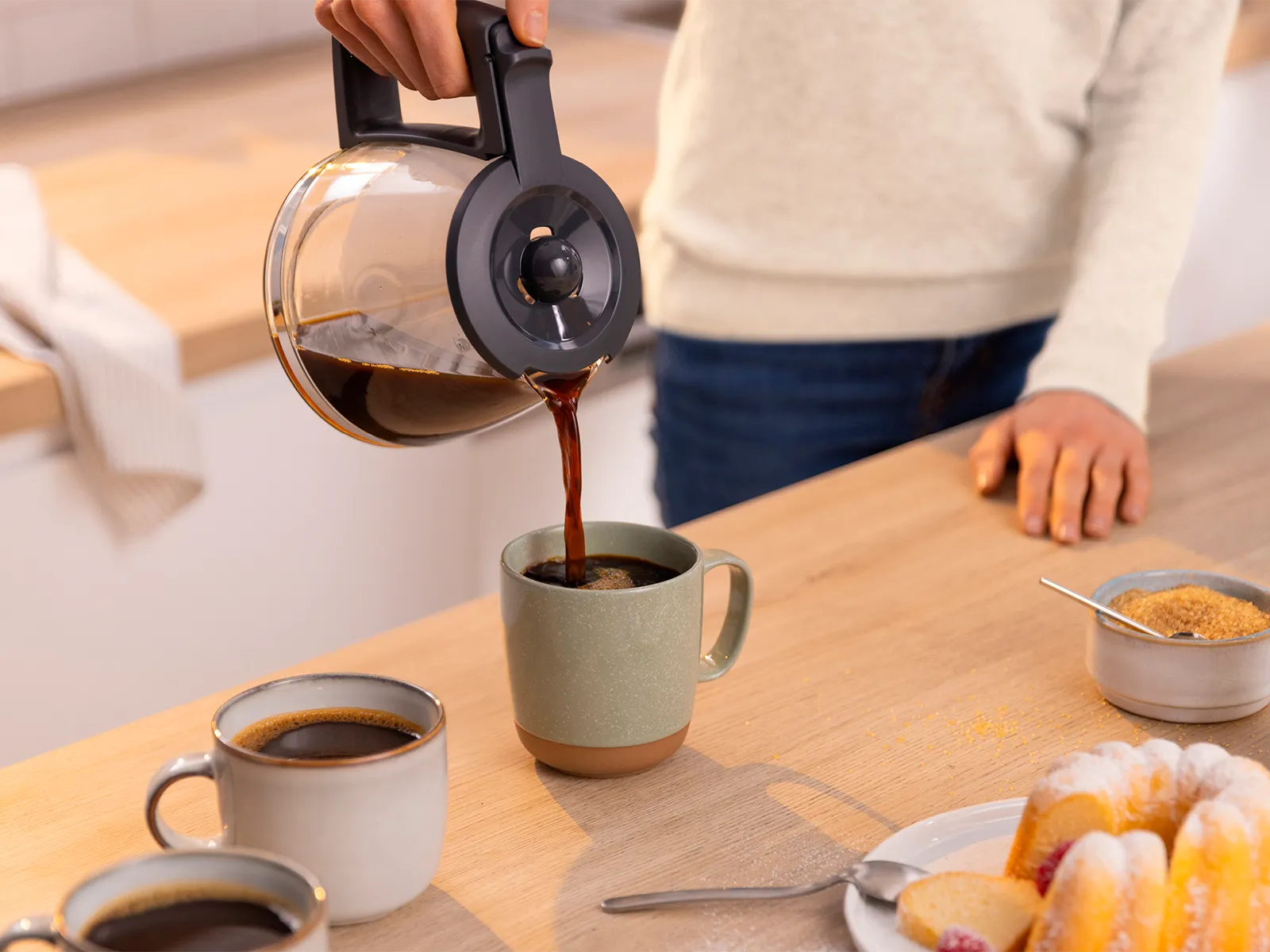 Person pouring coffee into cup from glass jug coffee maker.