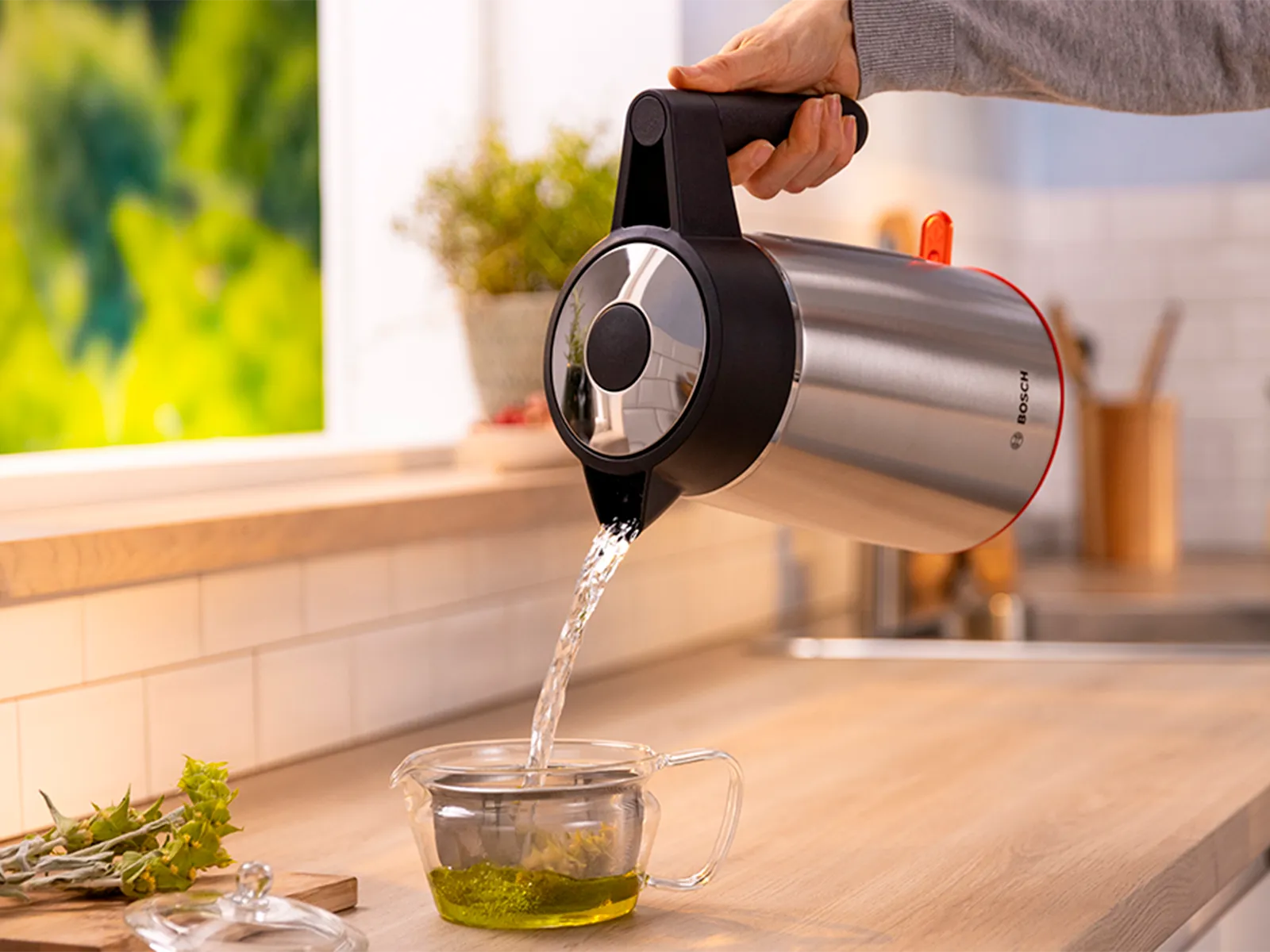 Water being poured from MyMoment kettle into glass mug with mint tea leaves.