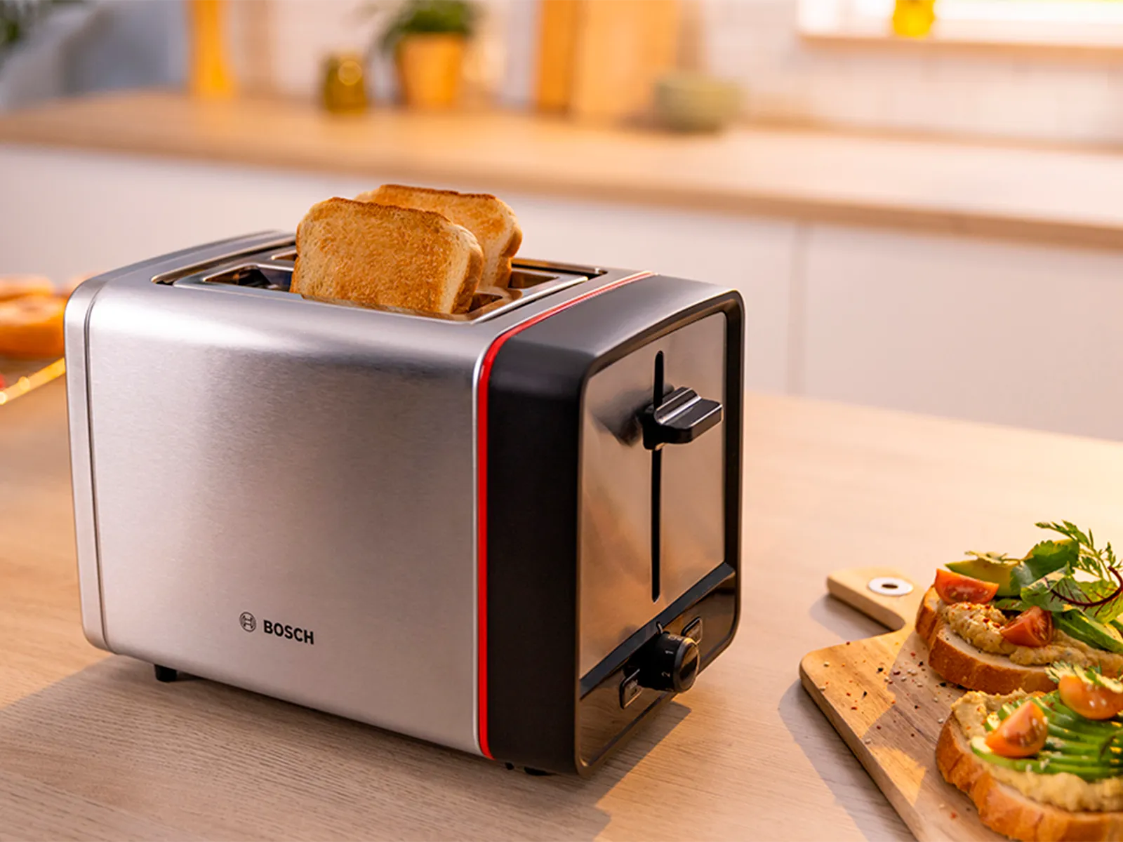 Stainless steel toaster with slices of toast next to a board with toasted topped with salmon and avocado on kitchen counter.