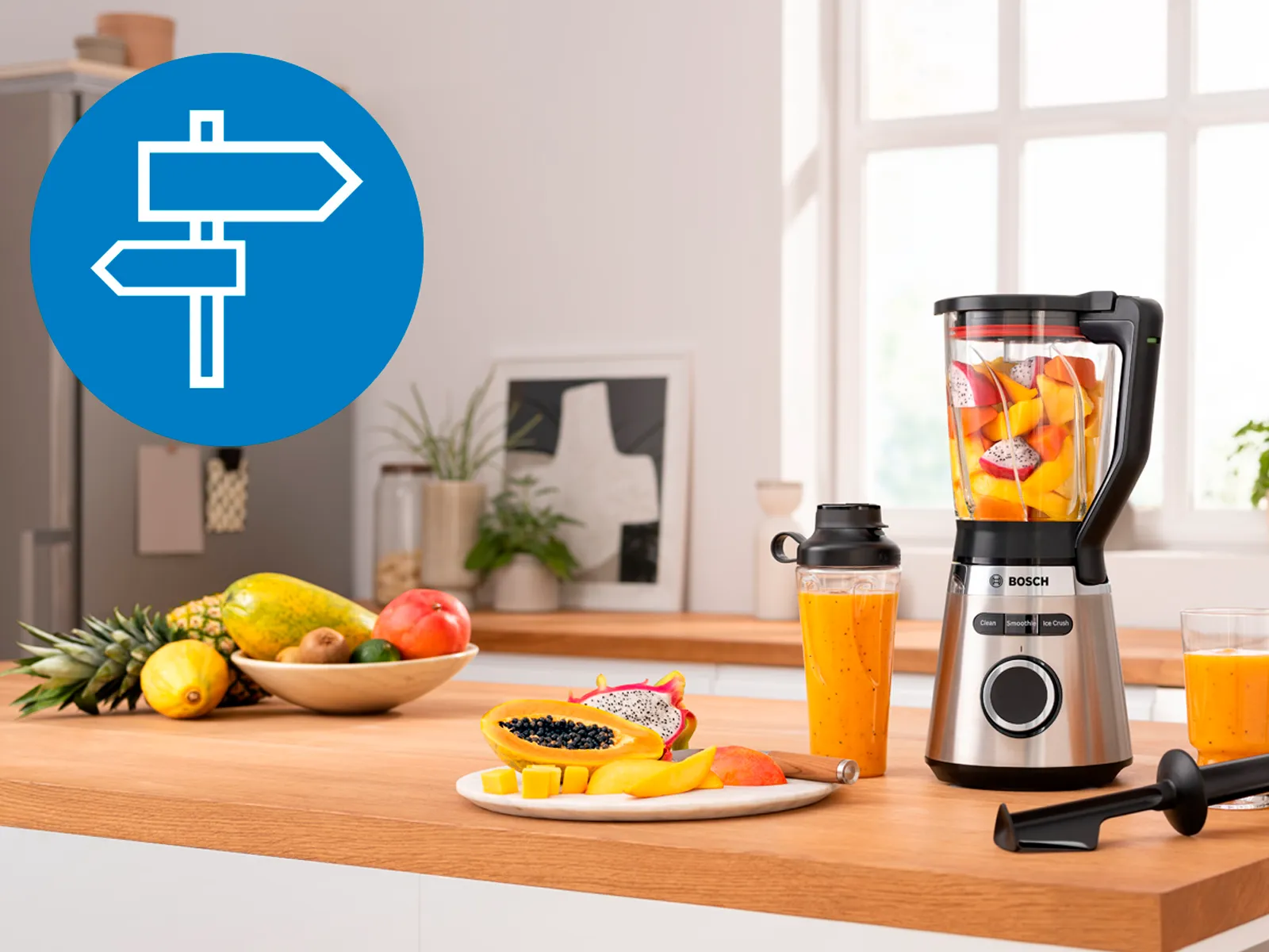 Bosch blender filled with fresh fruit, next to a to-go bottle and a glass of smoothie, set in a bright kitchen.