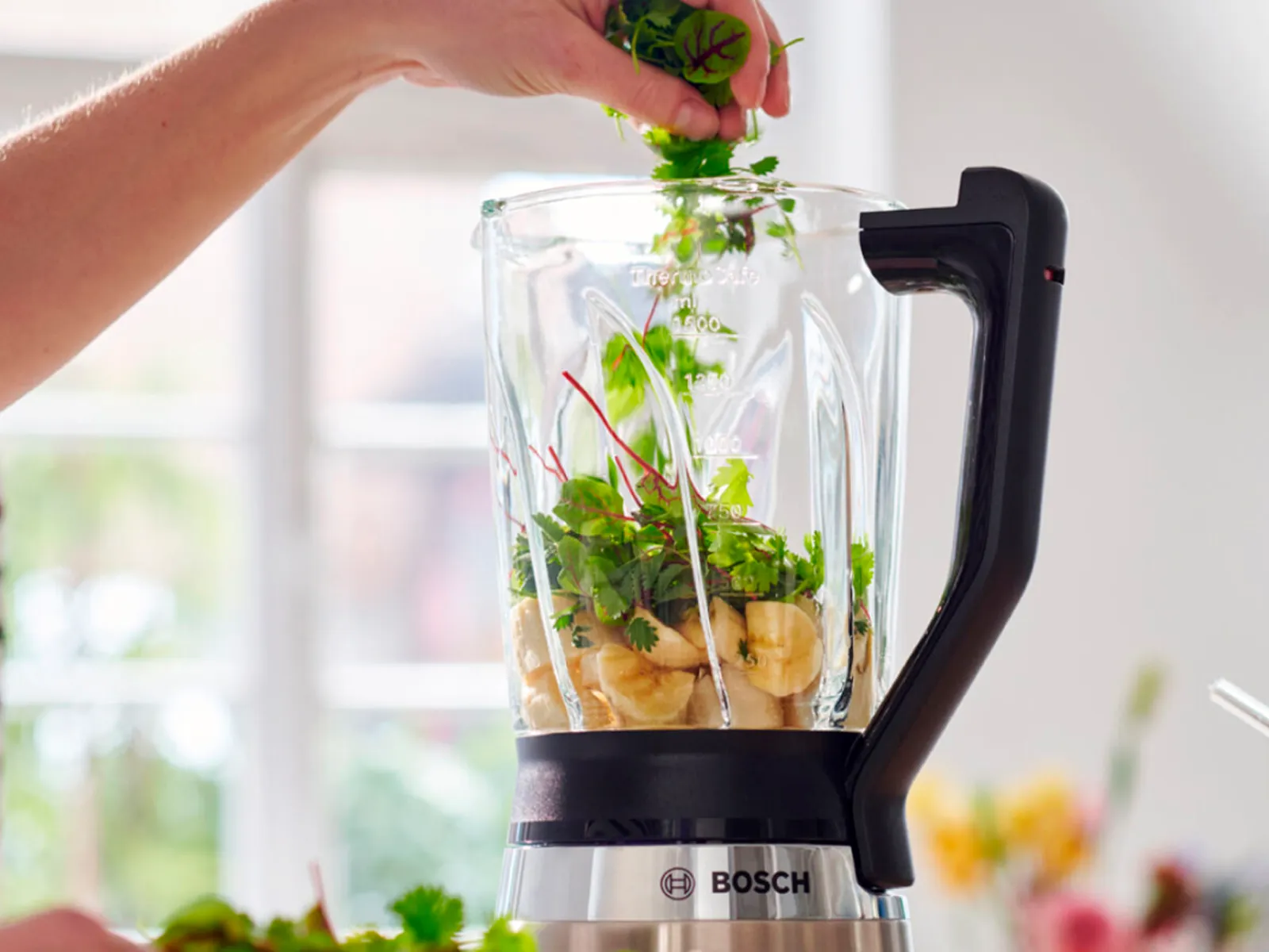 Bosch blender napunjen bananama i svježim začinskim biljem, savršen za pripremu zdravih smoothija i hranjivih miješavina kod kuće.