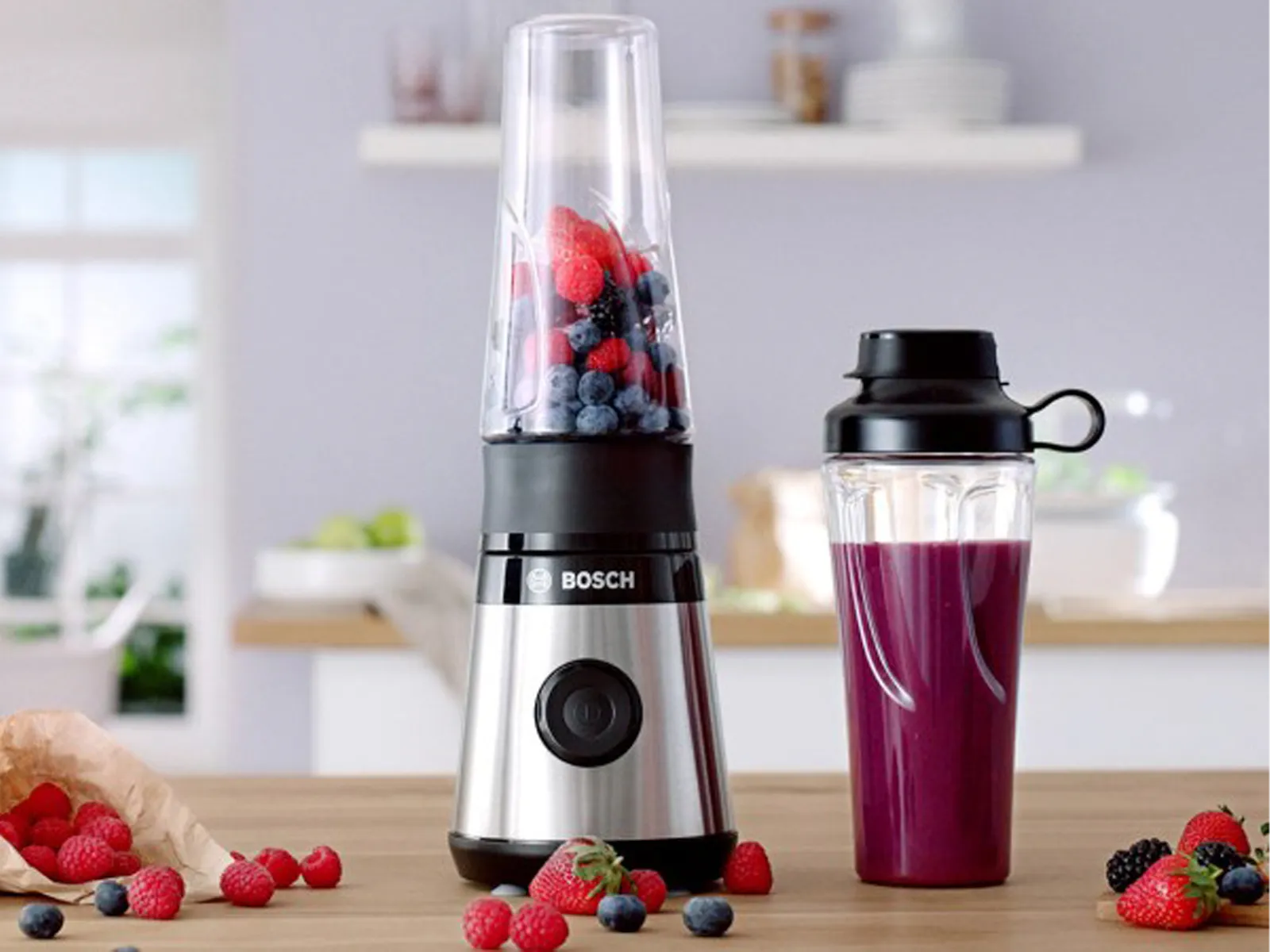 Miniblender VitaPower Serija 2 s crvenim voćem i bocom To-Go ispunjenom smoothiejem na kuhinjskom police.