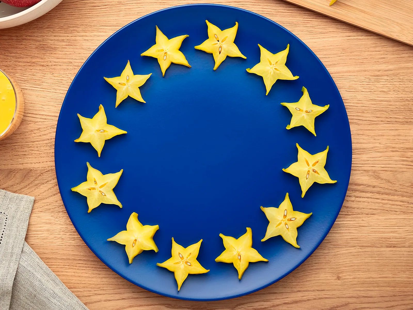 Kriške žutog zvjezdastog voća na plavom tanjuru stvaraju prikaz europske zastave.