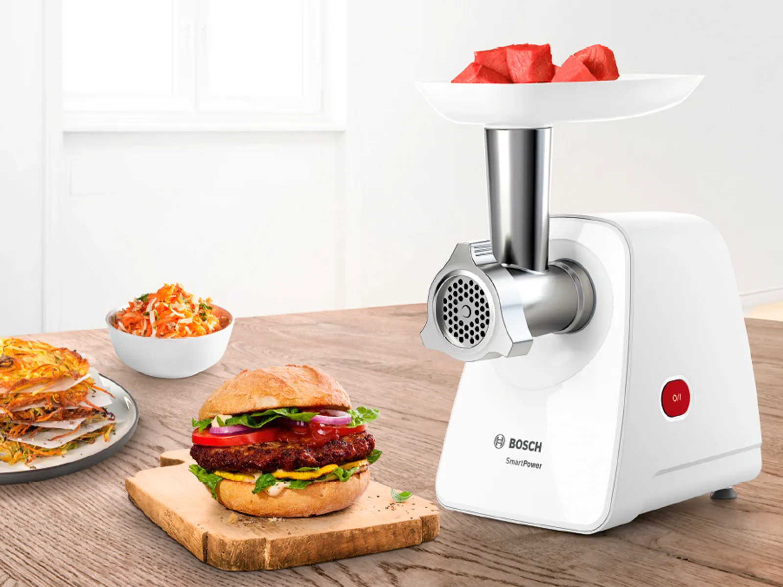 Tocătorul de carne SmartPower cu carne în tavă, lângă un burger aşezat pe un blat de bucătărie, alături de boluri cu sosuri şi salate.