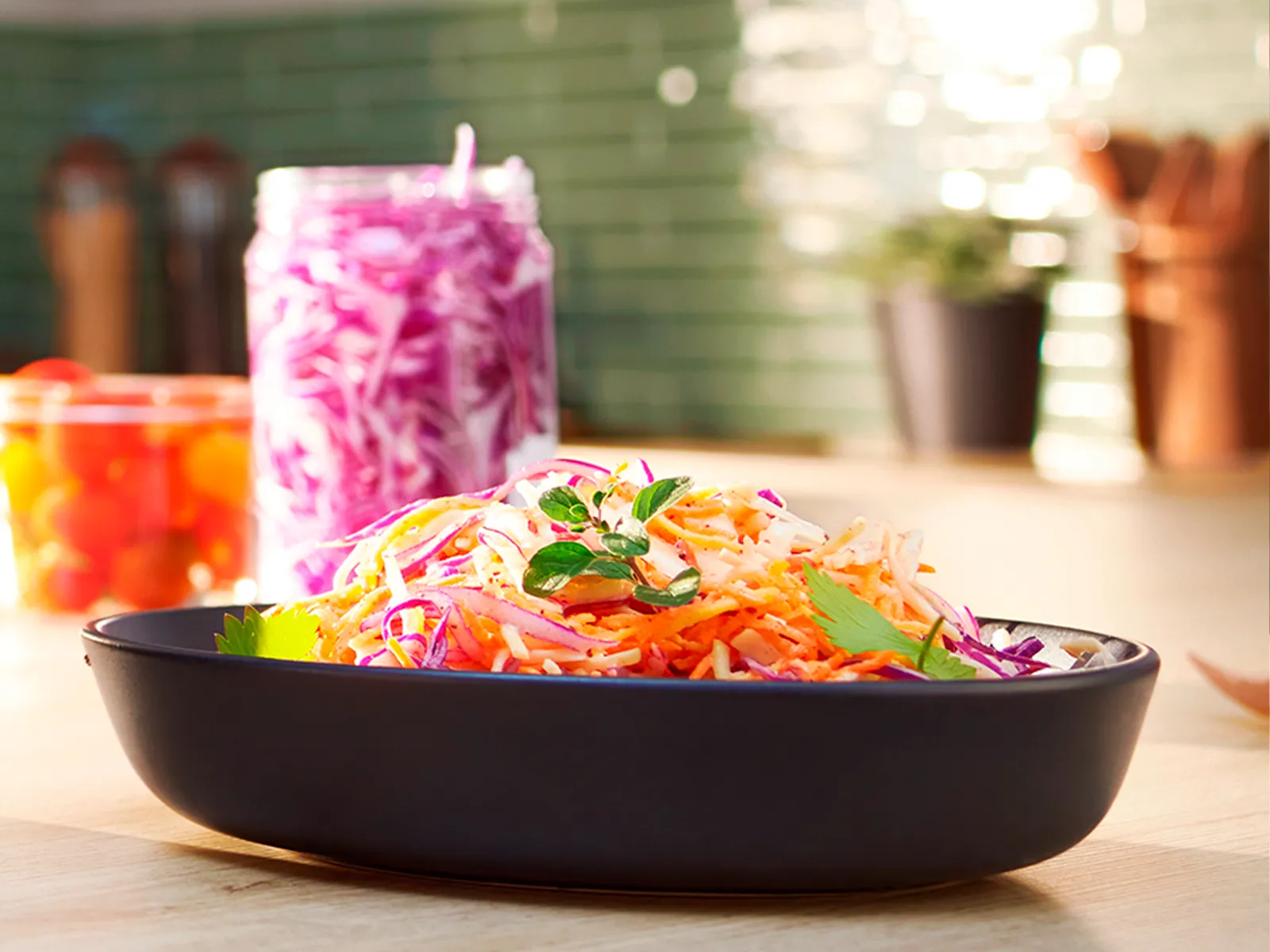 Un bol cu morcovi răzuiţi şi un borcan cu varză tocată pe un blat de bucătărie.